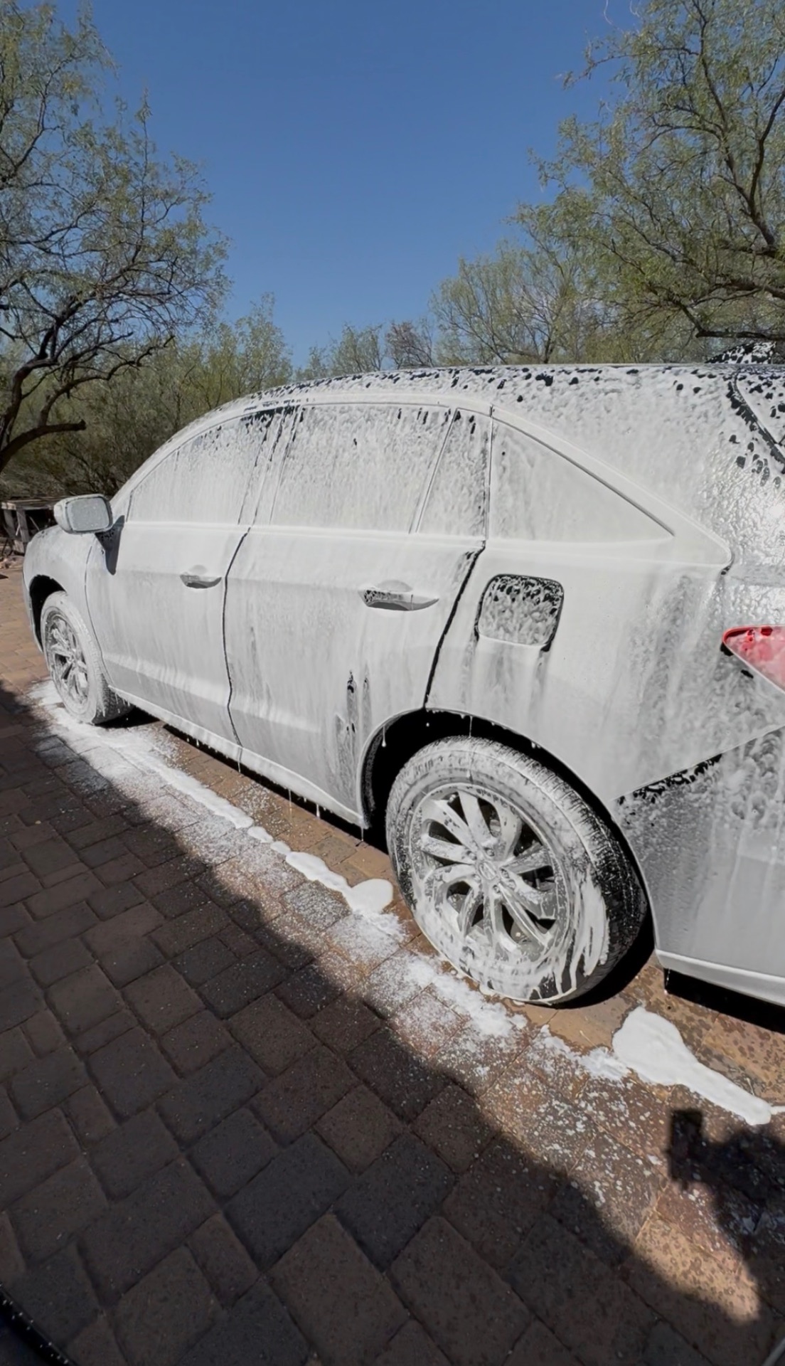 A white sedan covered in thick foam wash during a mobile detail in Tucson